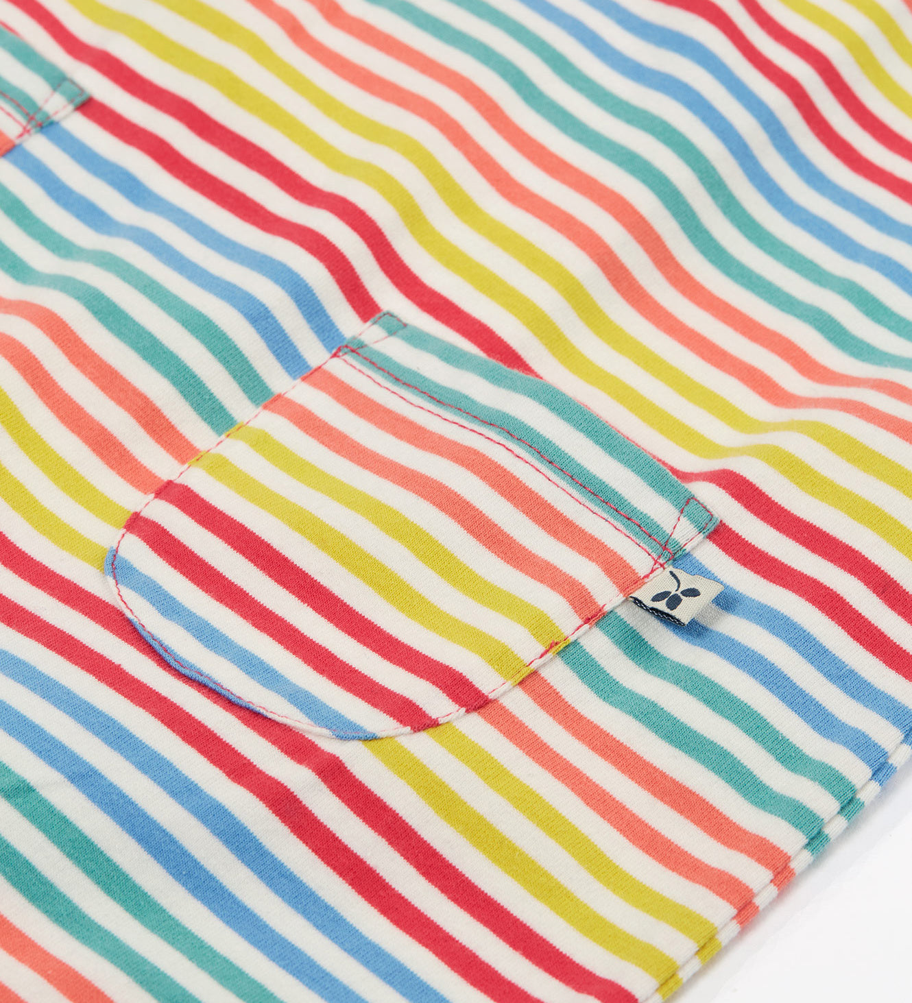 Close up of the Frugi kids cornflower rainbow stripe playsuit showing the small pocket detail on the front on striped organic cotton fabric.