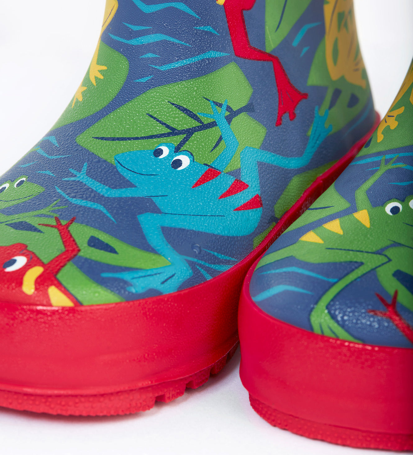 A close up of the bottom of the Frugi kids puddle buster wellington boots. Showing the the red trim and playful frog print detail on navy natural rubber material.