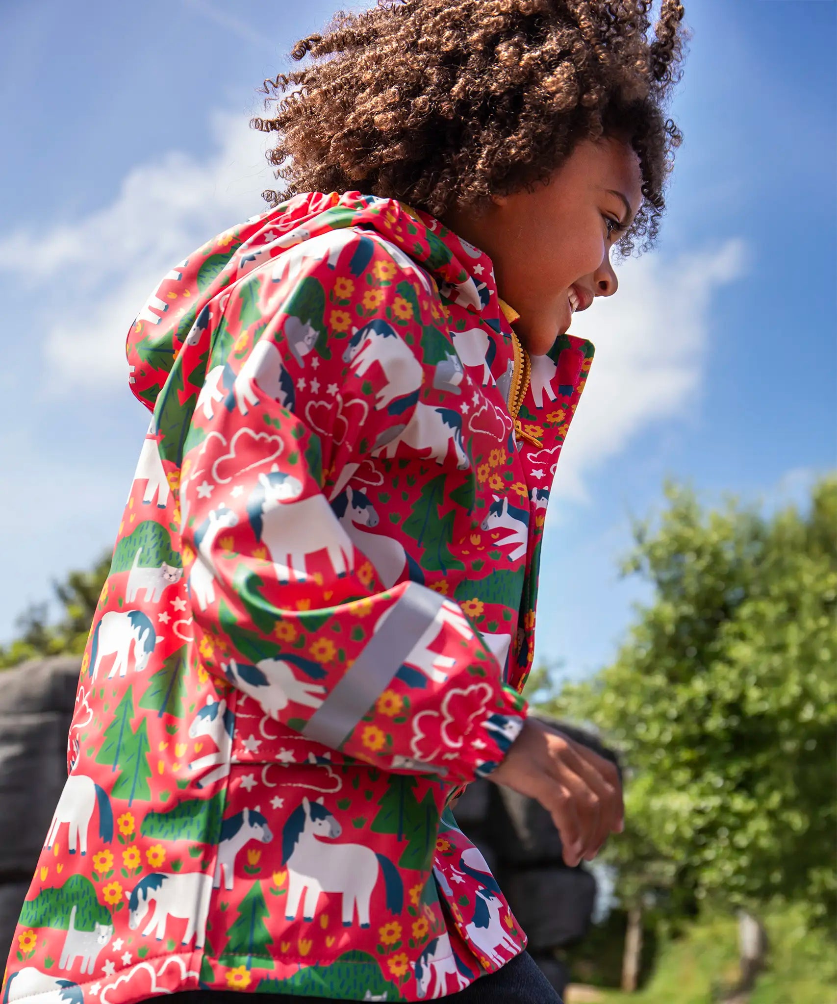 Child wearing Frugi waterproof puddle buster coat in pink purrfect ponies print showing the reflective strips on the wrist are of the arms. 