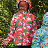 Child wearing Frugi waterproof puddle buster coat in pink purrfect ponies print with the hood up.