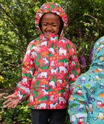 Child wearing Frugi waterproof puddle buster coat in pink purrfect ponies print with the hood up.