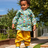 Child wearing Frugi waterproof puddle buster coat in blue terrific tractors  print with yellow puddle buster trousers and matching terrific tractor wellington boots. 
