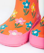 A close up of the bottom of the Frugi kids puddle buster wellington boots. Showing the the pink trim and playful flower print detail on orange natural rubber material.