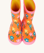 A top down view of the Frugi kids puddle buster wellington boots Showing the the pink trim and playful flower print detail on orange natural rubber material. 