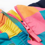 A close up of the Frugi rainbow check snow and ski salopettes showing the pink zip attaching the shoulder straps and bib to the trousers.
