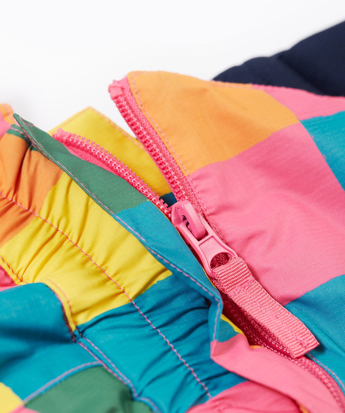 A close up of the Frugi rainbow check snow and ski salopettes showing the pink zip attaching the shoulder straps and bib to the trousers.