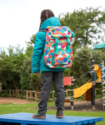 View of the back of a child wearing the Frugi kids 3 in 1 rambler coat in boat blue rhubarb check with a colourful Frugi Trail Blazing fun frenzy backpack on her back.