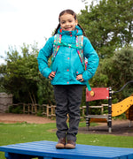 Child wearing the Frugi kids 3 in 1 rambler coat in boat blue rhubarb check with a Frugi Trail Blazing fun frenzy backpack on her back.