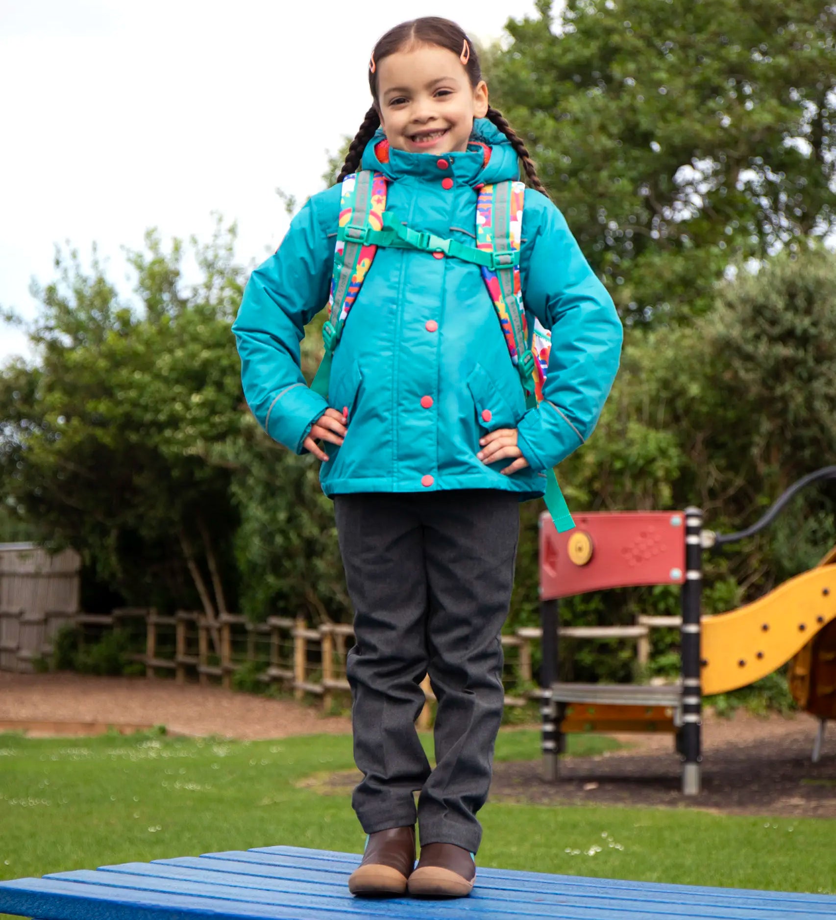 Child wearing the Frugi kids 3 in 1 rambler coat in boat blue rhubarb check with a Frugi Trail Blazing fun frenzy backpack on her back.