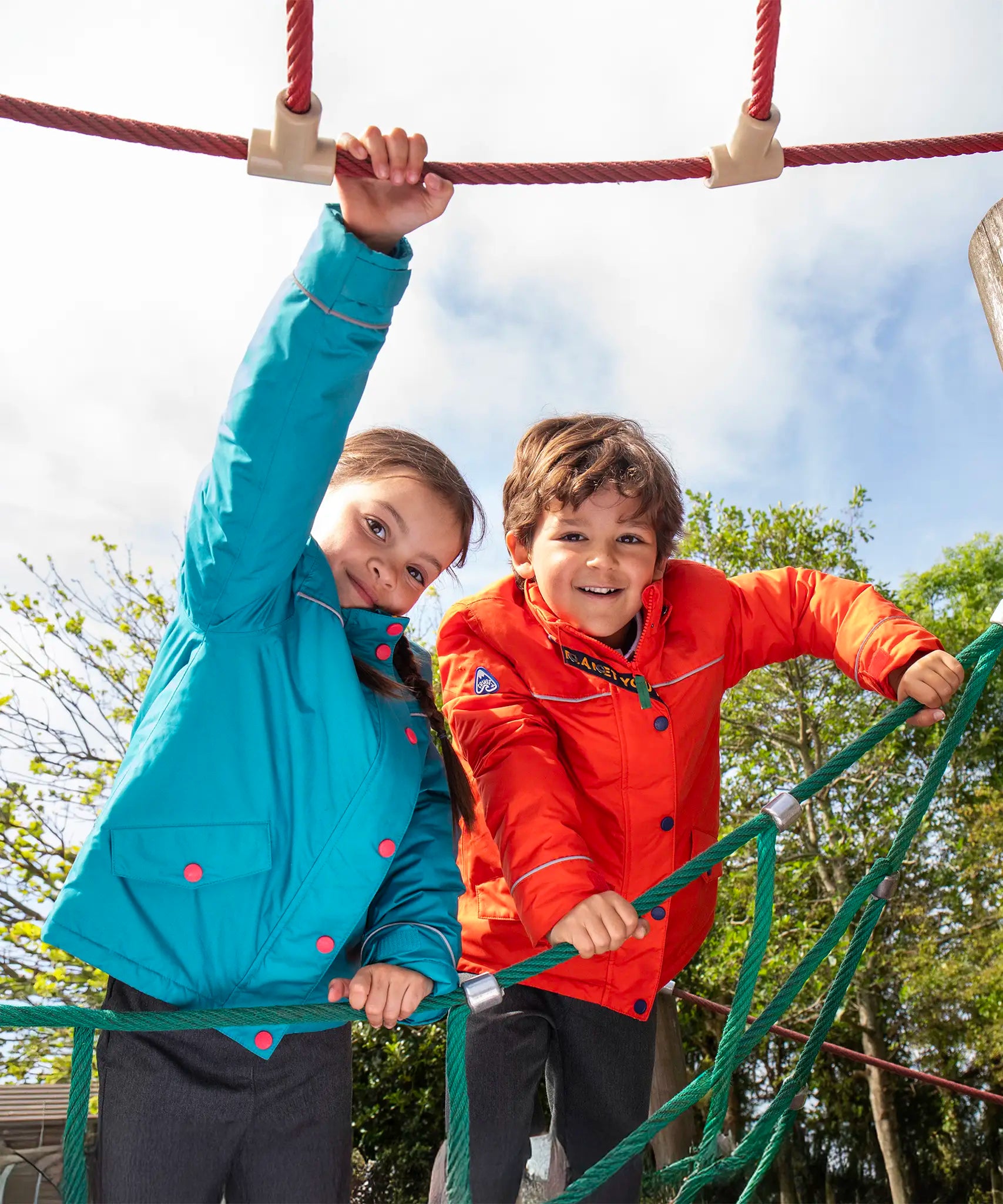 Two children wearing the Frugi kids 3 in 1 rambler coats, one in fire orange , one in boat blue.