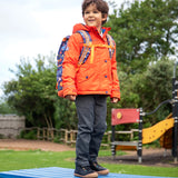 Child wearing the Frugi kids 3 in 1 rambler coat in fire orange upon a star with a Frugi backpack on his back.