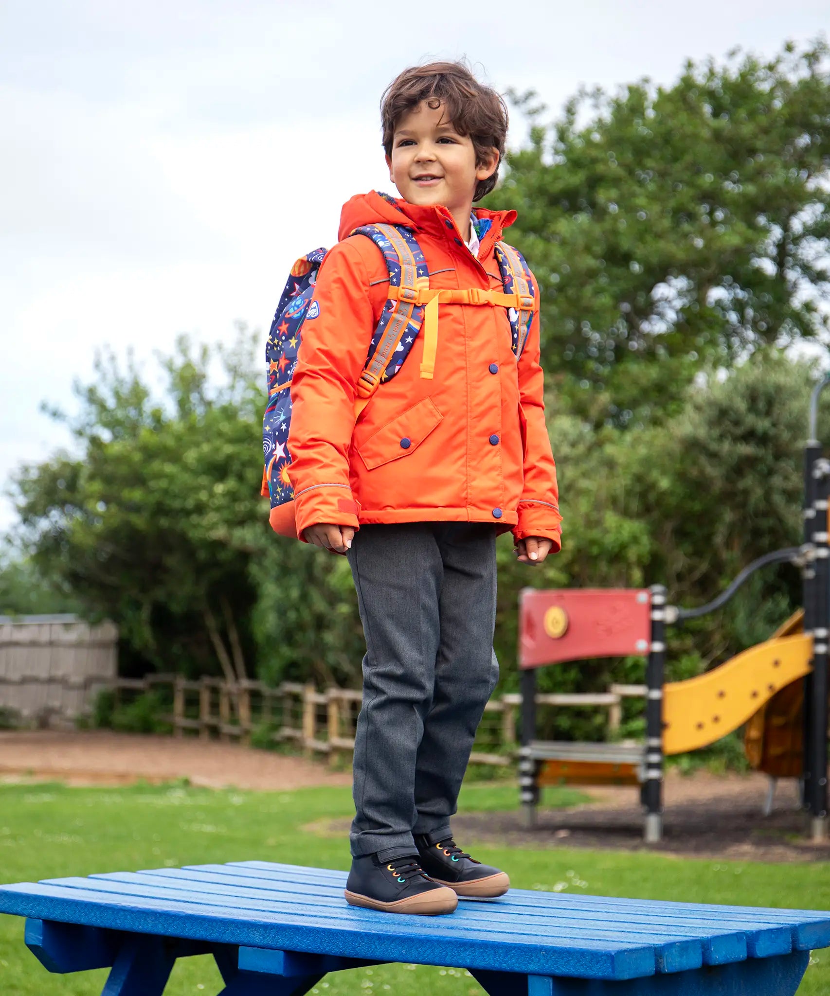 Child wearing the Frugi kids 3 in 1 rambler coat in fire orange upon a star with a Frugi backpack on his back.