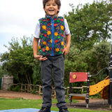 Child wearing the blue star print fleece gilet from the Frugi kids 3 in 1 rambler coat in fire orange upon a sta.