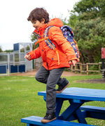 Child wearing the Frugi kids 3 in 1 rambler coat in fire orange upon a star with a Frugi backpack on his back.