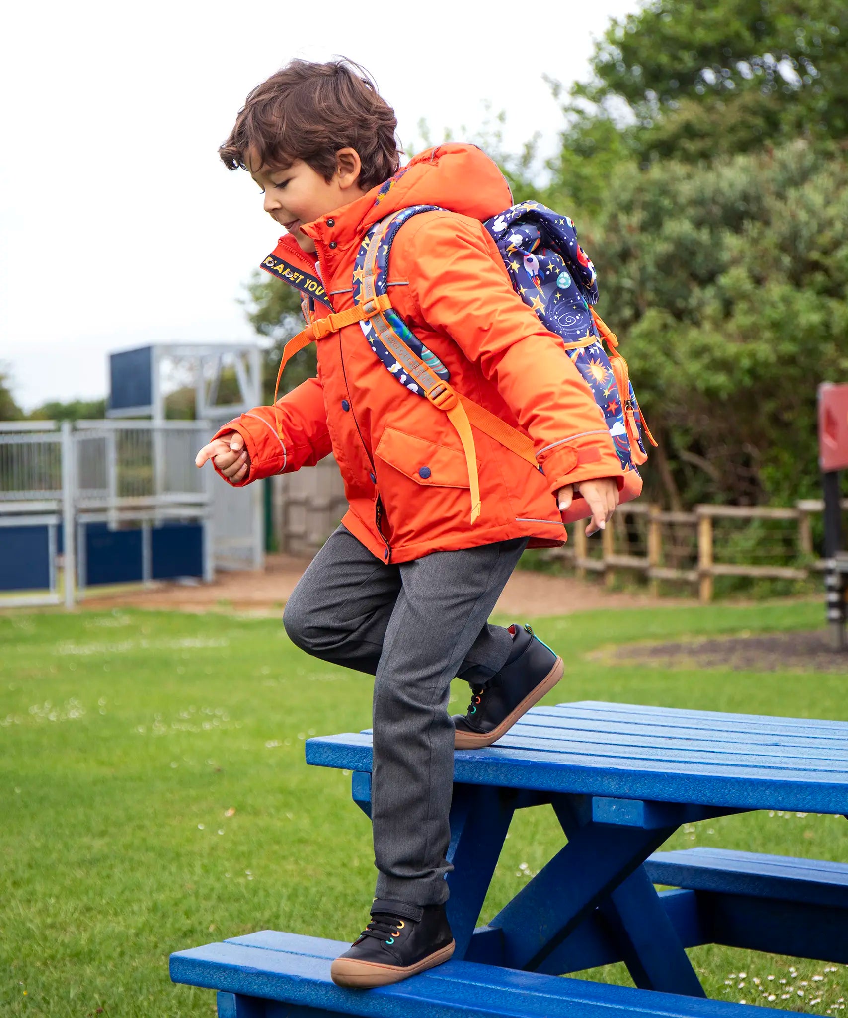 Child wearing the Frugi kids 3 in 1 rambler coat in fire orange upon a star with a Frugi backpack on his back.