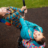Two children in a playground wearing Frugi coats. One is wearing the Frugi kids 3 in 1 rambler coat in boat blue rhubarb.
