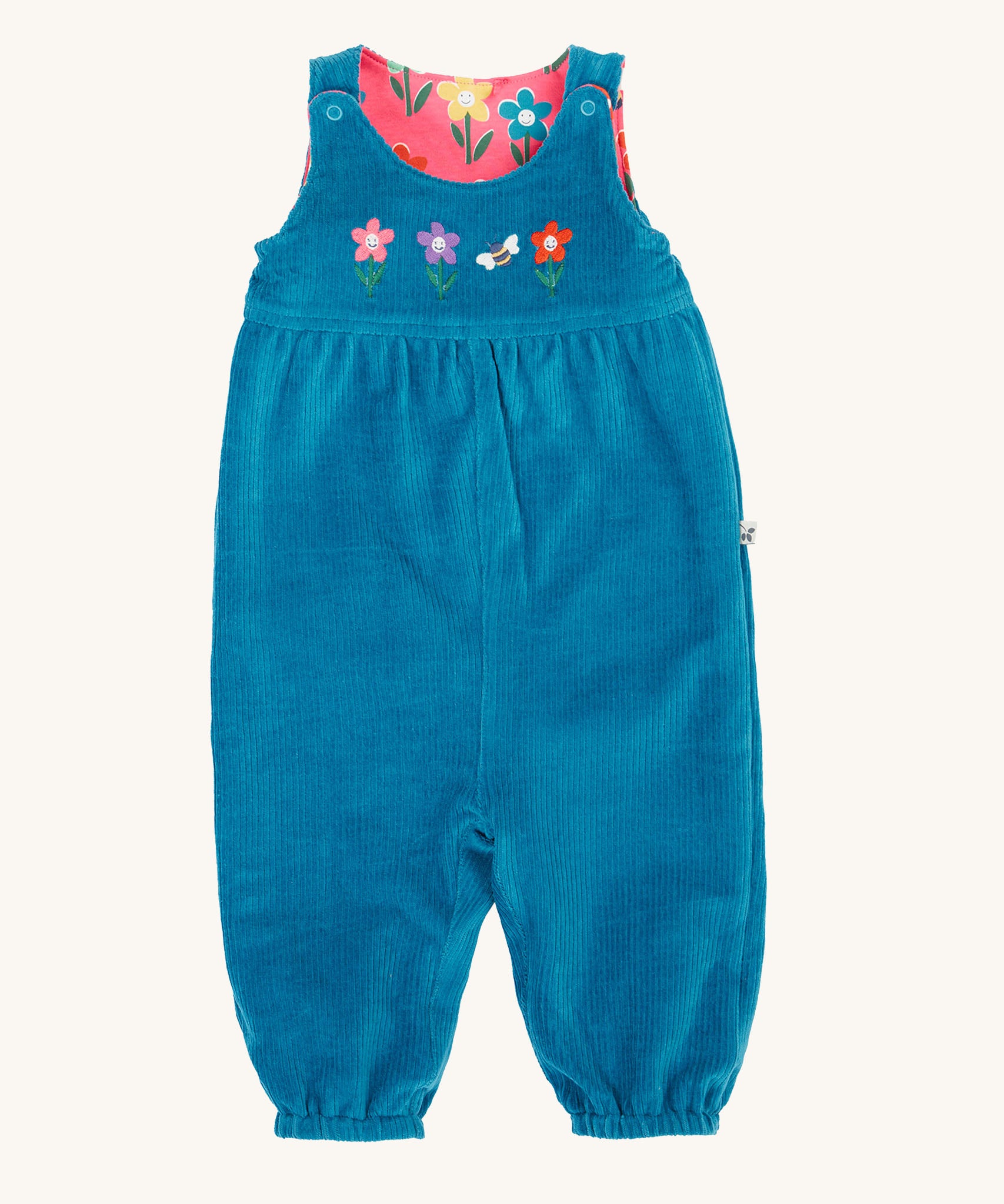 Frugi kids reversible helen dungarees in boat blue. A 100% GOTS organic cotton dungaree in blue corduroy with playful flower appliques on the front. Features popper fasteners on the shoulder straps and cuffed  ankles.