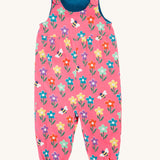 Frugi kids reversible helen dungarees in fun flowers. A 100% GOTS organic cotton pink dungaree playful flower prints. Features popper fasteners on the shoulder straps and cuffed ankles.