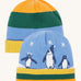 Frugi reversible voyager hat in penguin/ rainbow. A GOTS organic cotton cosy hat with a cute penguin design on blue with a yelow, green and orange striped ribbed trim and a matching bold stripe on the reverse side. 