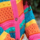 A close up of a child wearing the Frugi kids rowe rainbow cardigan in rainbow/pointelle showing the button and soft knit detail.