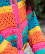 A close up of a child wearing the Frugi kids rowe rainbow cardigan in rainbow/pointelle showing the button and soft knit detail.