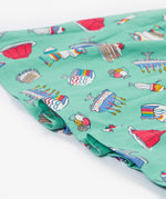 A close up of the Frugi kids lets bake Morwenna skater dress. Showing the different cakes, ice cream, puddings and light frill on light green organic cotton fabric