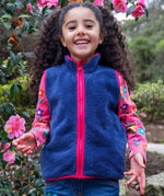 A child wearing the Frugi navy fleece gilet from the snapdragon/navy waterproof rambler 3 in 1 coat. A removable fleece gilet in navy with a pink zip and trim. 