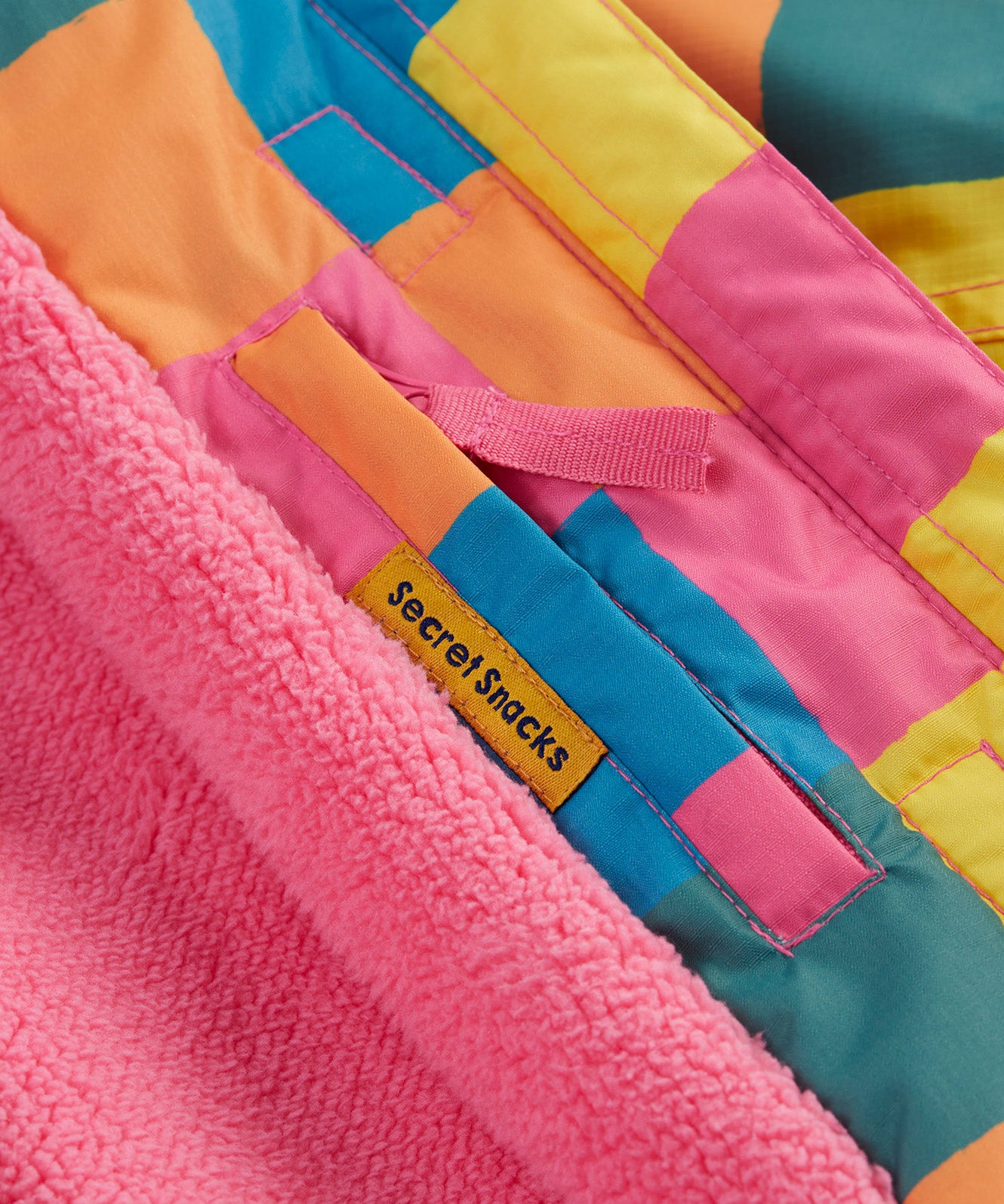 A close up of the Frugi kids snow and ski coat in rainbow check showing the hidden pocket on the inside and pink fleece detail
