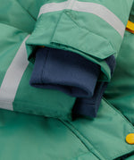 A close up of the Frugi kids snow and ski coat in green with a mountain scene print. Showing the extended navy arm cuffs for warmth and velcro detail for size adjustment.  