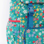 A close up of the Frugi kids trail blazing backpack in wild woods. Showing blue buckle for the flip top  and bottle holder detail