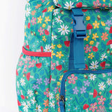A close up of the Frugi kids trail blazing backpack in wild woods. Showing blue buckle for the flip top  and bottle holder detail
