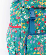 A close up of the Frugi kids trail blazing backpack in wild woods. Showing blue buckle for the flip top  and bottle holder detail