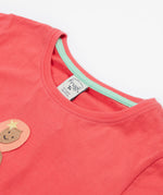 A close up of the top half of the Frugi Tamara t-shirt showing the light turquoise trim on the inside of the neck on light pink organic cotton  fabric