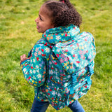 A child standing outside with a Frugi trailblazing backpack in wildwoods backpack on the back. A Light green backpack with woodland inspired prints all over. Features 2 buckle fasteners on the lid, a small zipped compartment on the front and 2 bottle holders.