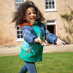 A child happily outside wearing the Frugi Snow & Ski Coat - Iguana Colourblock. The image shows the zipper at the front open