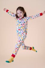 A child jumping in the air and wearing the Frugi Zelah fun guys all in one zip suit available at Babipur. A GOTS organic cotton all in one suit light pink with a playful woodland inspired prints and red cuffs. Features a full length zip.