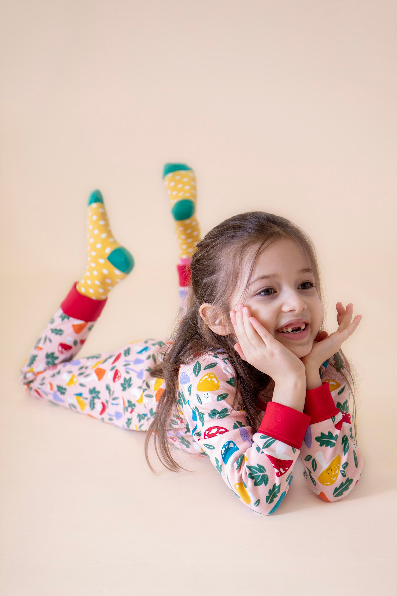 A child lying down and wearing the Frugi Zelah fun guys all in one zip suit available at Babipur. A GOTS organic cotton all in one suit light pink with a playful woodland inspired prints and red cuffs.