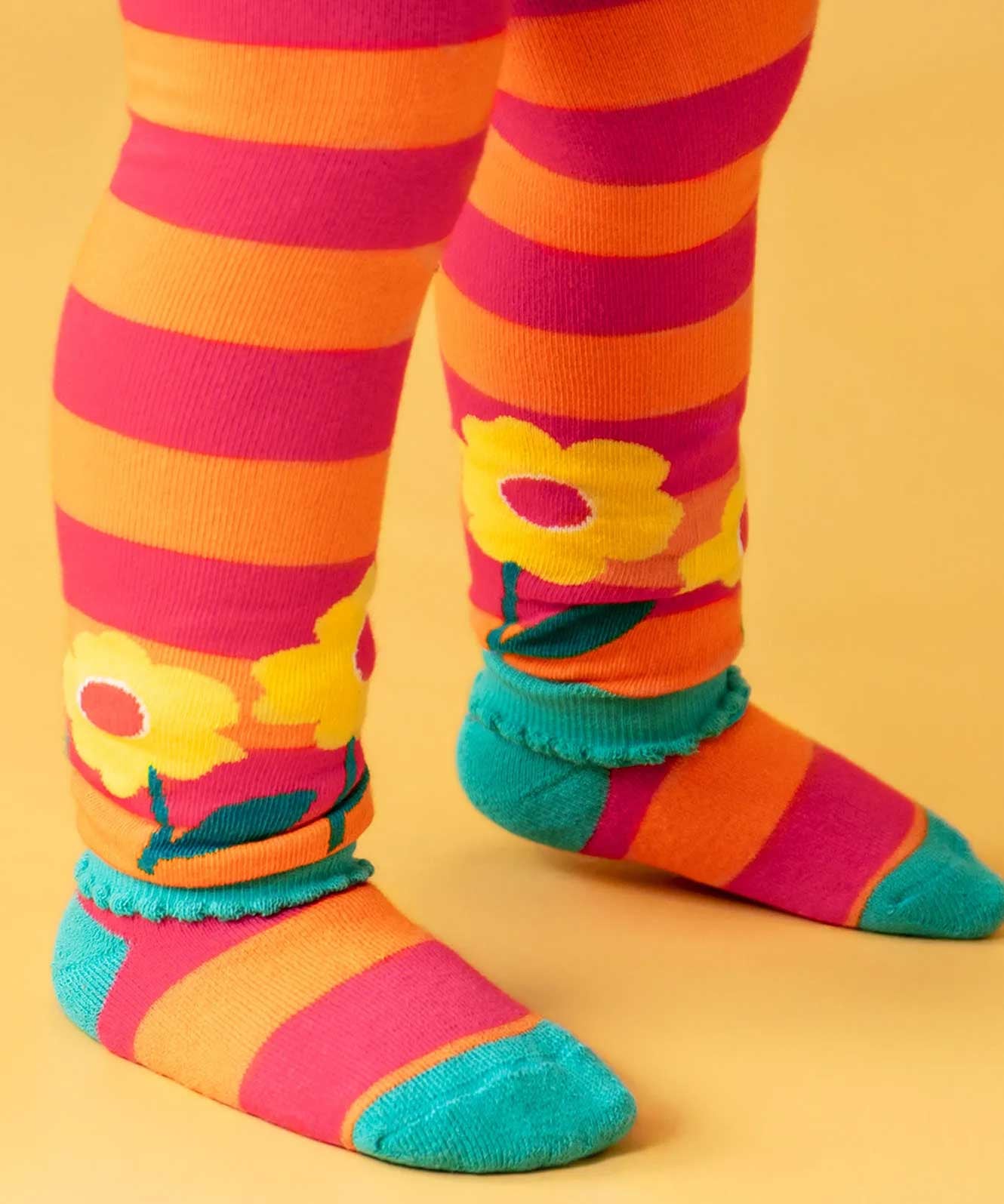 Close up of the bscalopped edges on the cuffs of the Frugi orange and pink striped knitted leggings. The bottoms have yellow flowers around them.