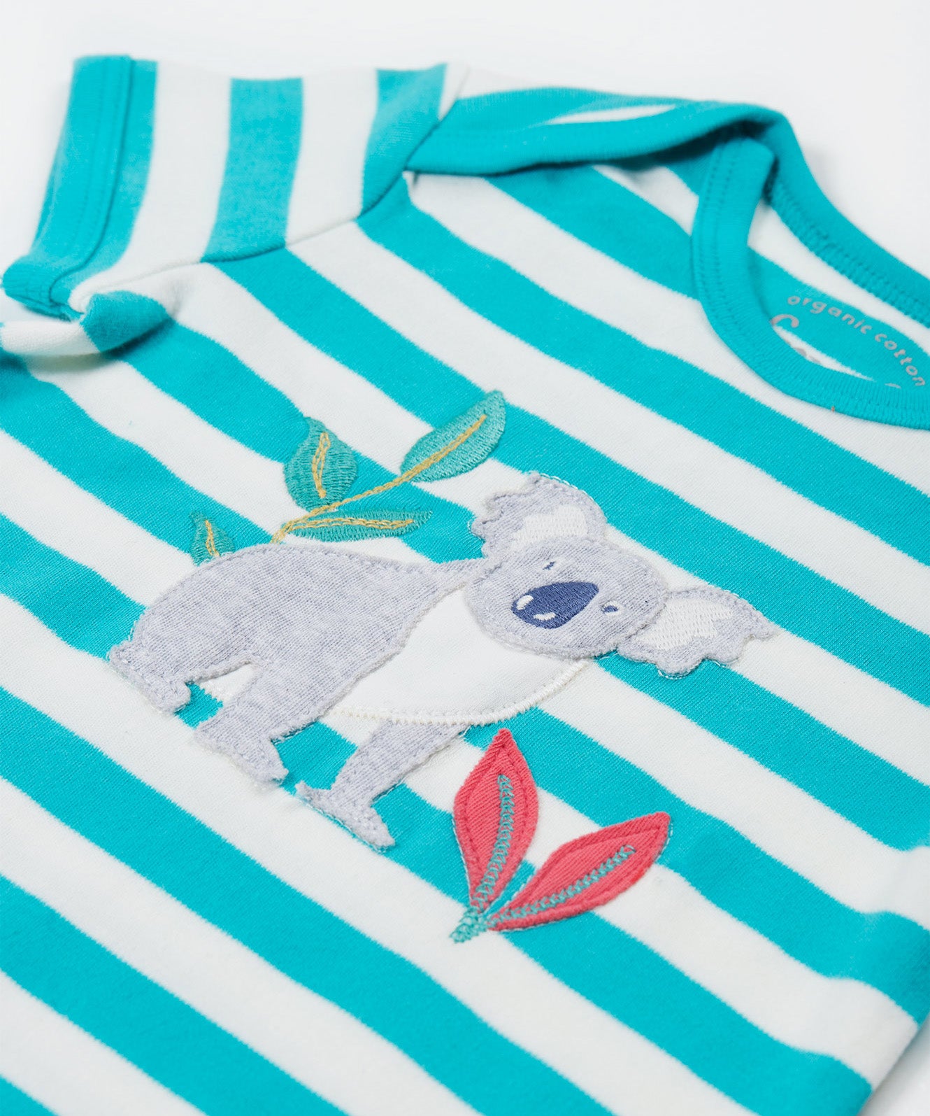 A close up of the Frugi Koala rue romper showing the grey koala applique next to pink leaves and a bamboo shoot on blue and white striped organic cotton fabric