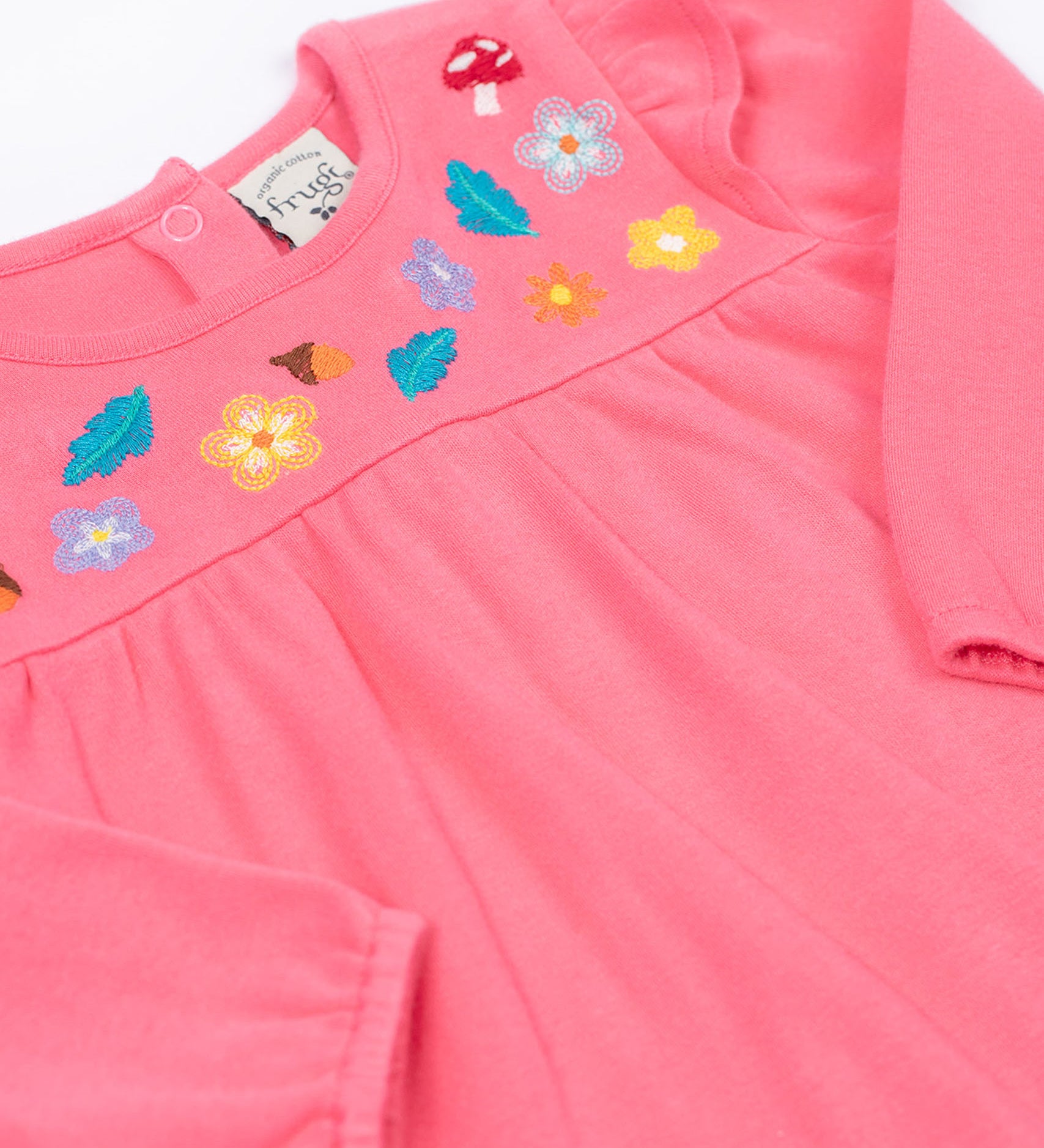 A close up of the Frugi kids kyla outfit in tulip/wild woods showing the long sleeves pink top with frilled shoulders. Features woodland themed embroidery. 
