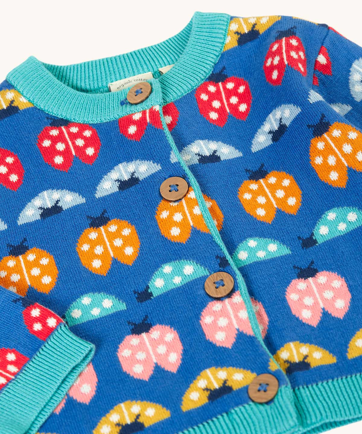 A clos up of the front of the Frugi blue knitted fair isle children's cardigan with red, yellow,  blue orange and pink ladybirds all over. Button up organic cotton cardigan with four wooden buttons.