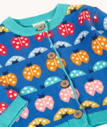 A clos up of the front of the Frugi blue knitted fair isle children's cardigan with red, yellow,  blue orange and pink ladybirds all over. Button up organic cotton cardigan with four wooden buttons.