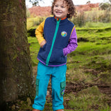 Child wearing the Frugi Lennox adventure trousers in boat blue organic cotton corduroy with a navy fleece gilet and long sleeved raglan top underneath.