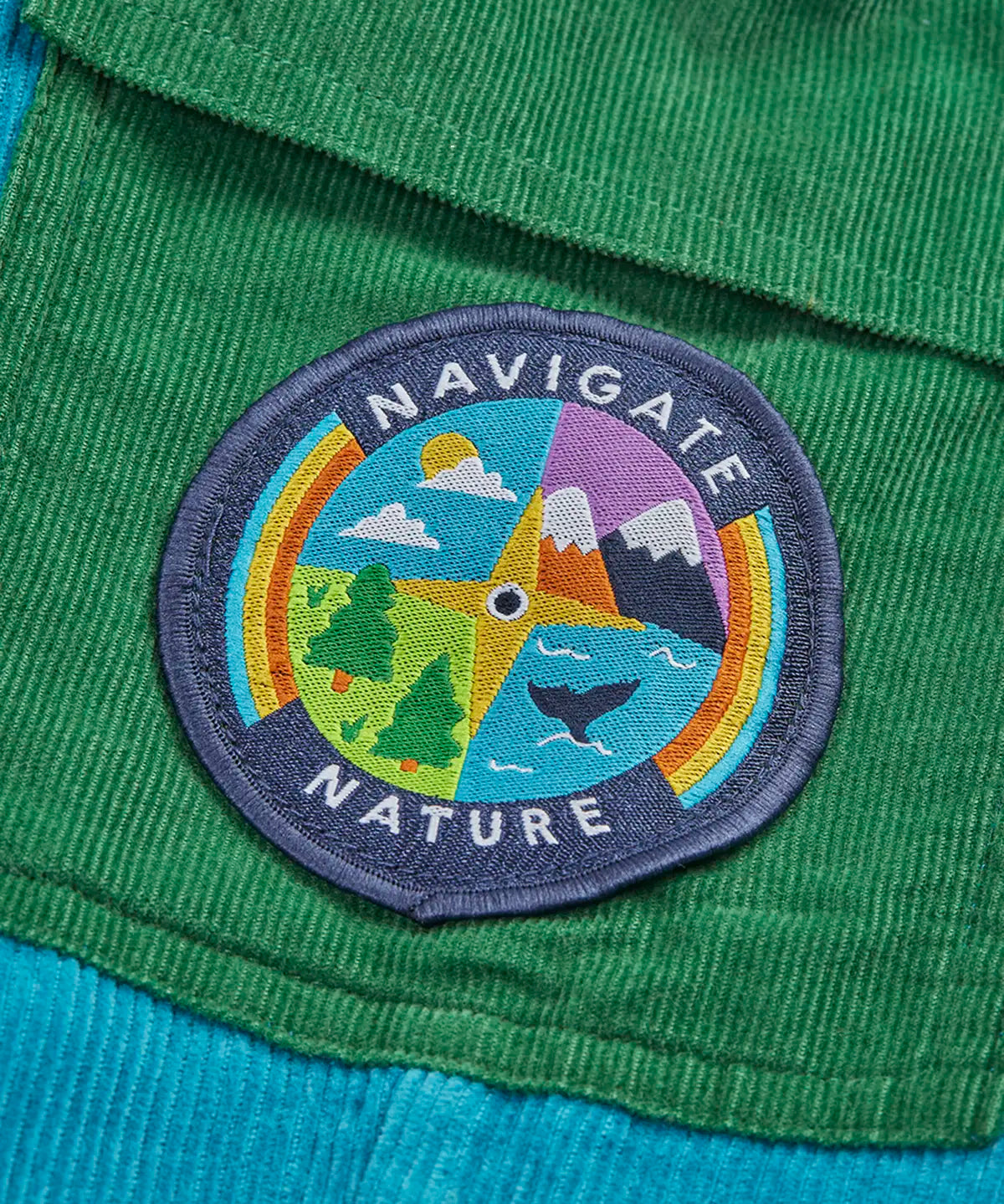 Frugi GOTS 100% organic cotton adventure corduroy trousers in blue showing a playful outdoor compass patch on green side pocket