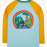 The back of the Frugi Children's Leo raglan long sleeved top. The body of the top is light blue with yellow gold coloured sleeves and a contrasting dark green neck collar. The large circular graphic on the back features the words out in the wild written on a river surrounded by land, trees, mountains all surrounded by a three colour rainbow.