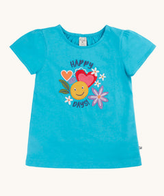 Frugi turquoise blue short puff sleeved children's t-shirt with happy days in navy blue font enveloping a graphic containing a yellow smiley face, pink and red heart and flowers.