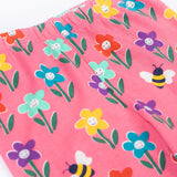 Frugi organic cotton kids Libby leggings with a fun flowers print on a pink background. The flowers are multi-coloured and have happy faces on them.