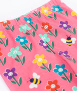 Frugi organic cotton kids Libby leggings with a fun flowers print on a pink background. The flowers are multi-coloured and have happy faces on them.