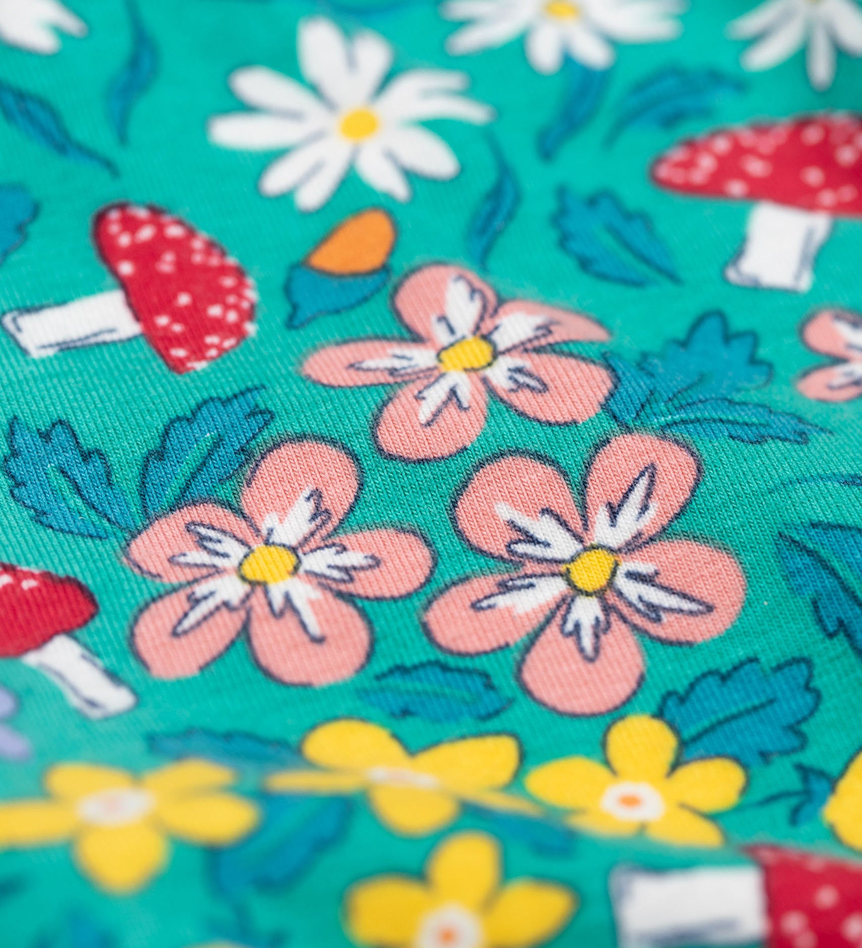 A close up of the print on the Frugi Libby leggings with a wild woods, botanical design on a green background. 