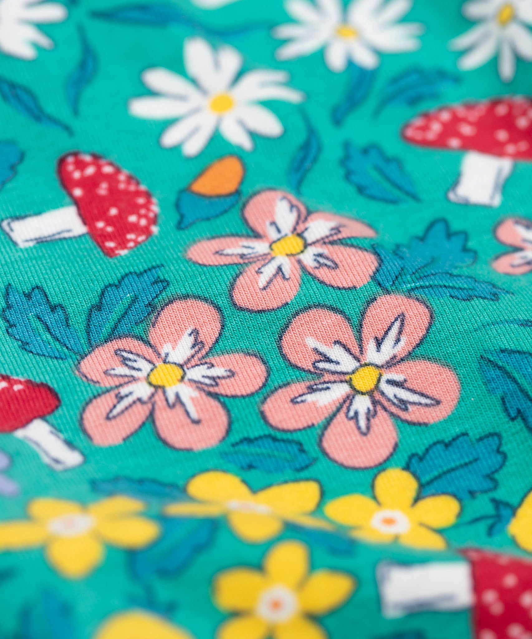 A close up of the print on the Frugi Libby leggings with a wild woods, botanical design on a green background. 